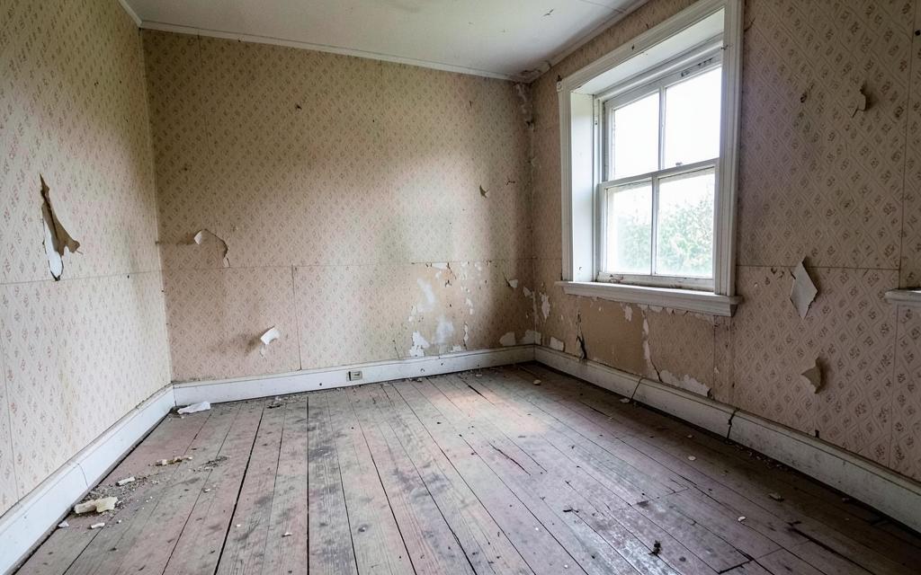 A run down room with peeling wallpaper and bare floorboards